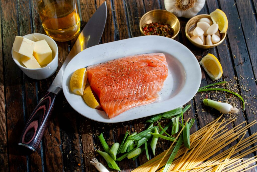 raw salmon on a plate with lemons with pasta, green onions, garlic, and butter surrounding